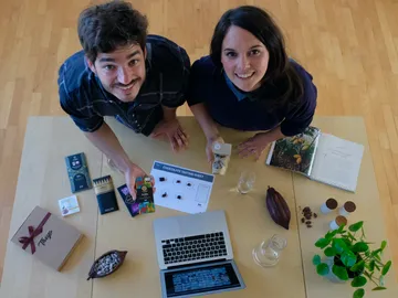 Two people smile across a table full of chocolate.