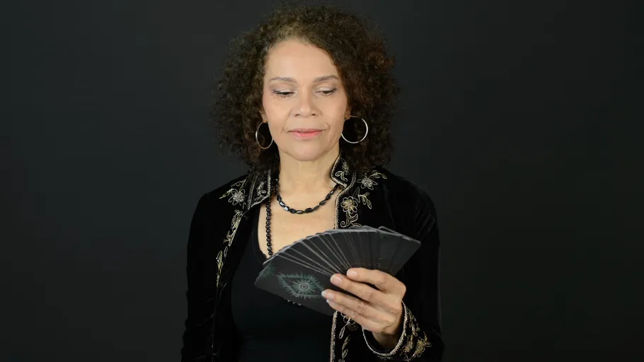 Woman holding tarot cards, black background.