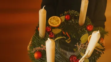 Candle wreath with oranges and ornaments held up.