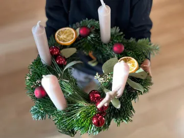Person hält festlichen Adventskranz drinnen.