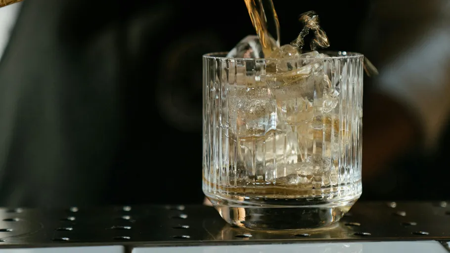 Cocktail wird in Glas mit Eis gegossen.