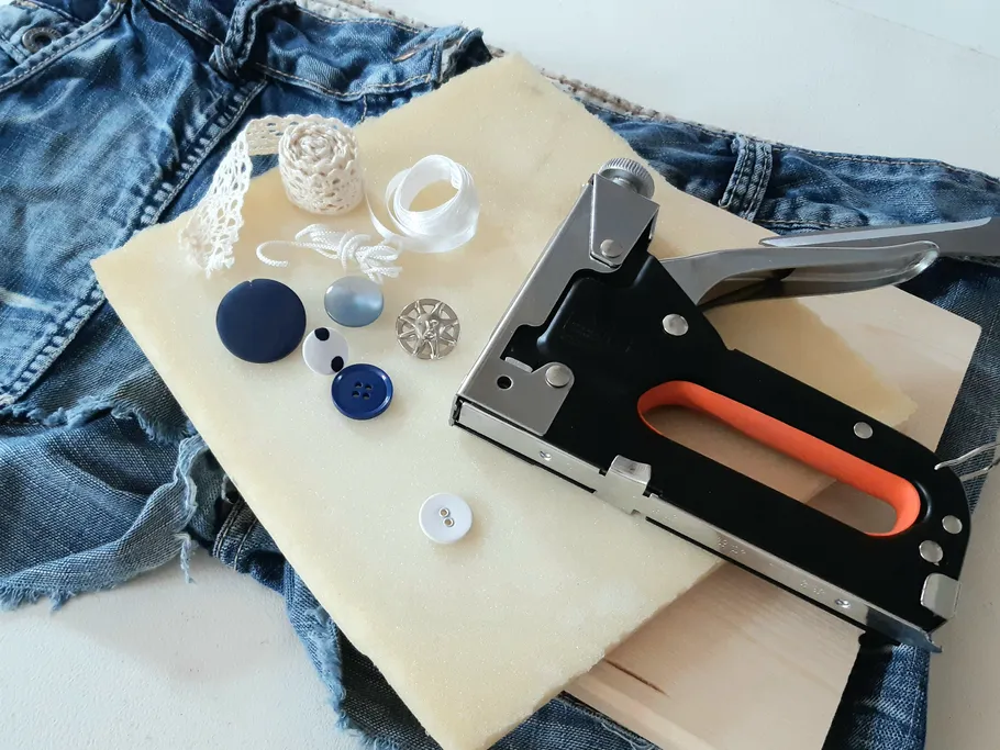 The stapler lies next to buttons and fabric on a white table.