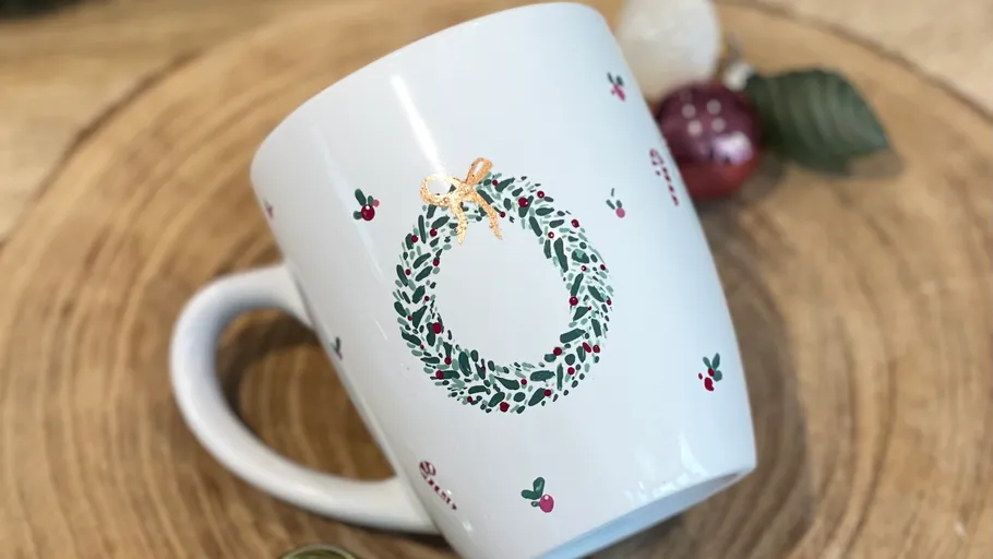 Weißer Becher mit Kranzdesign, Holzuntergrund.