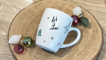 Tasse mit 'Let it snow' auf Holzuntersetzer.
