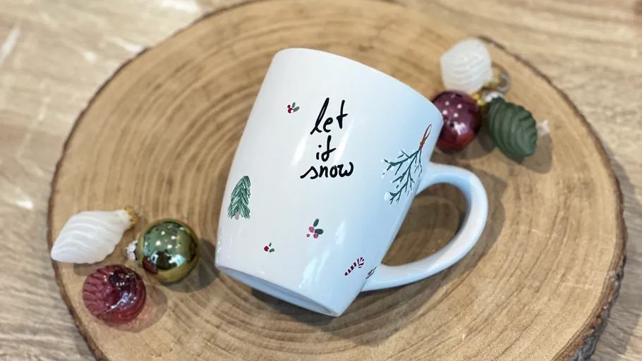 Mug with 'Let it snow' on wooden coaster.