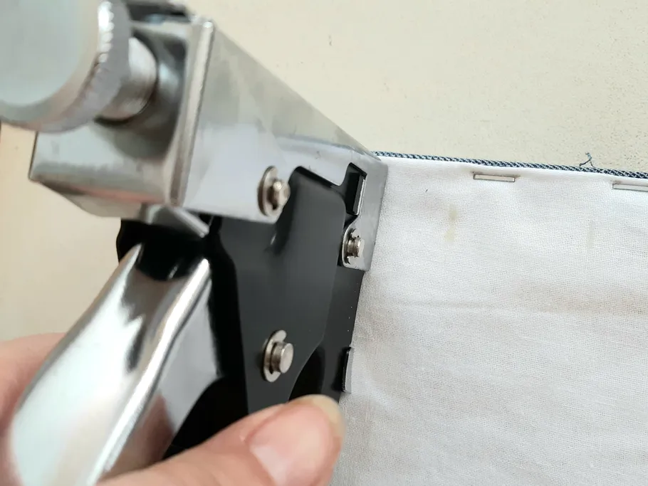 Stapler secures an edge of fabric to a surface.