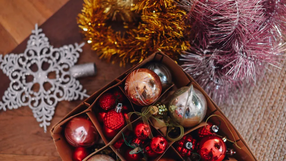 Box of Christmas ornaments with tinsel nearby.