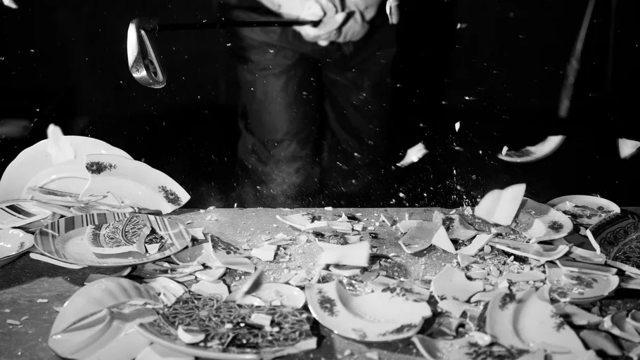 Person zerbricht Teller mit Golfschläger.