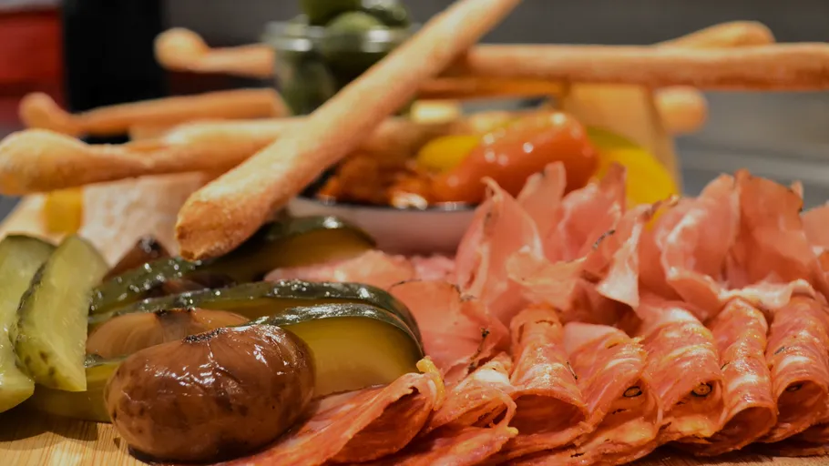 Charcuterie board with meats, breadsticks, and pickles.