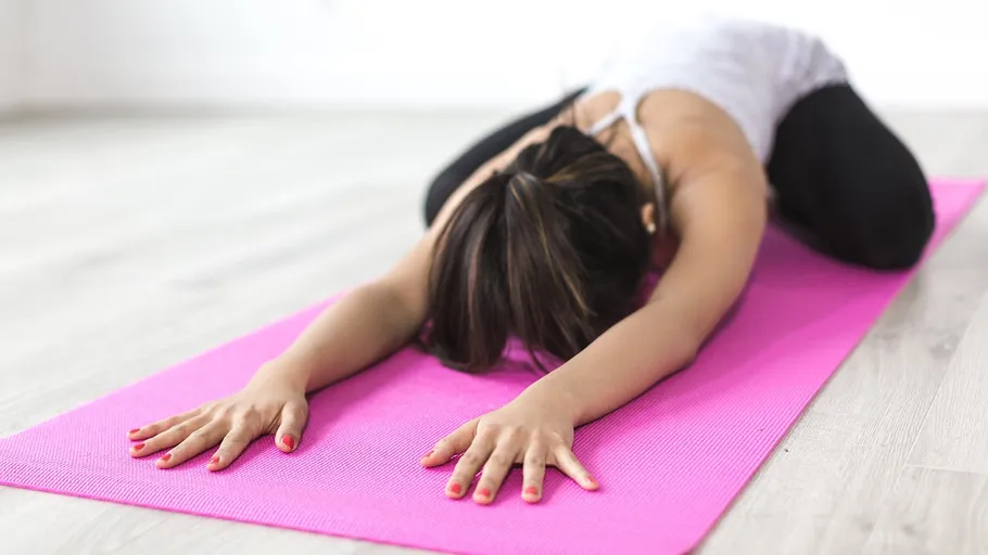 Person stretching on pink yoga mat indoors.