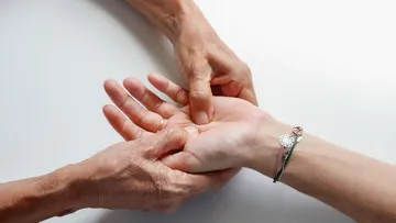 Zwei Hände massieren eine andere Hand auf Tisch.