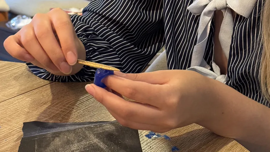 Person crafting with wax on wooden table.