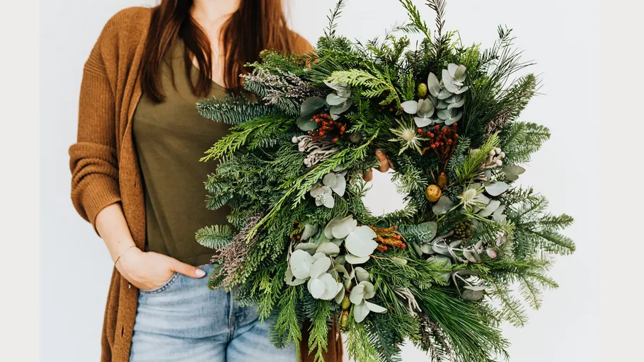 Person holding lush green holiday wreath.