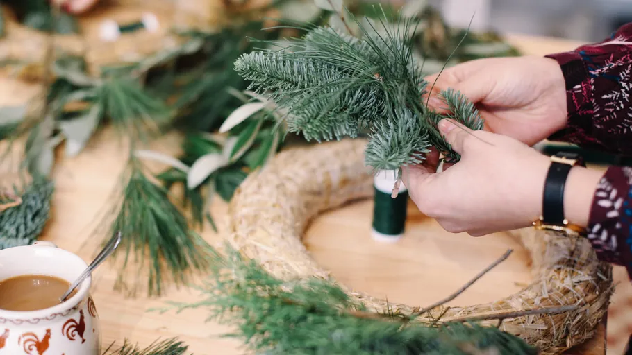 Hands crafting a wreath on table.