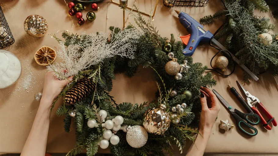 Person creating Christmas wreath on table.