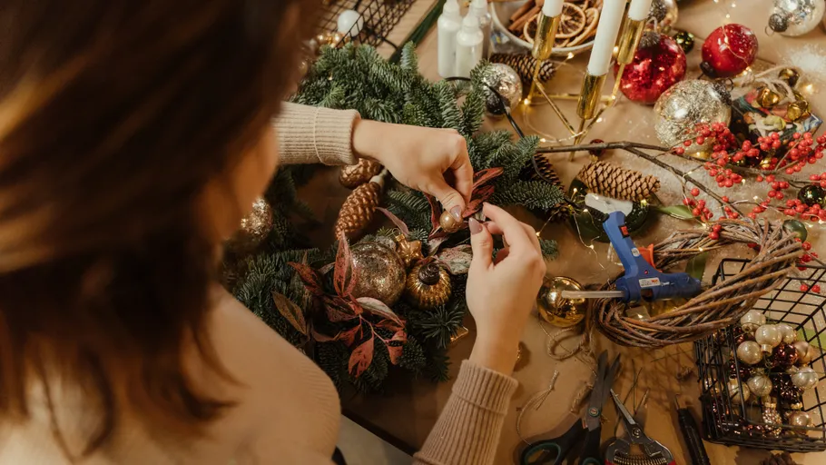 Person crafting a festive wreath on a table.
