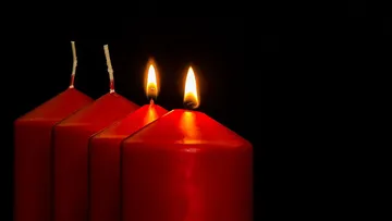 Vier rote Kerzen, zwei brennen, dunkler Hintergrund.