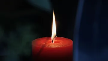 Rote Kerze brennt vor dunklem Hintergrund.