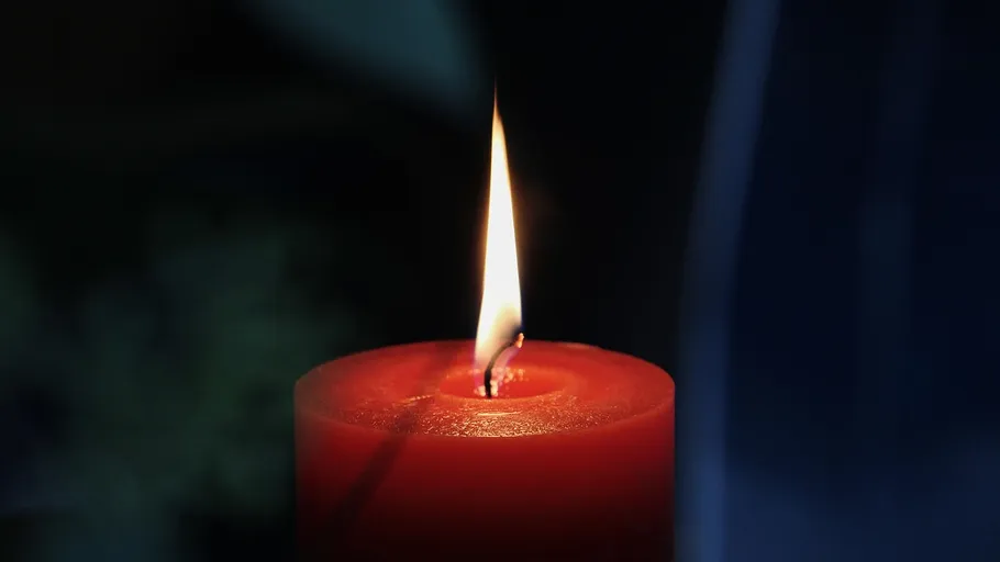 Rote Kerze brennt vor dunklem Hintergrund.
