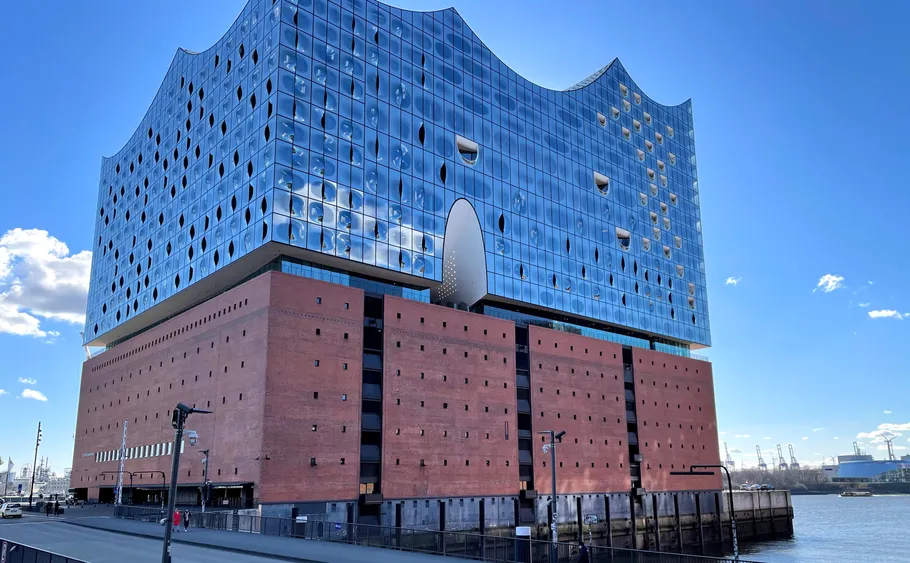 Modernes Konzerthaus am Wasser, sonniger Tag.