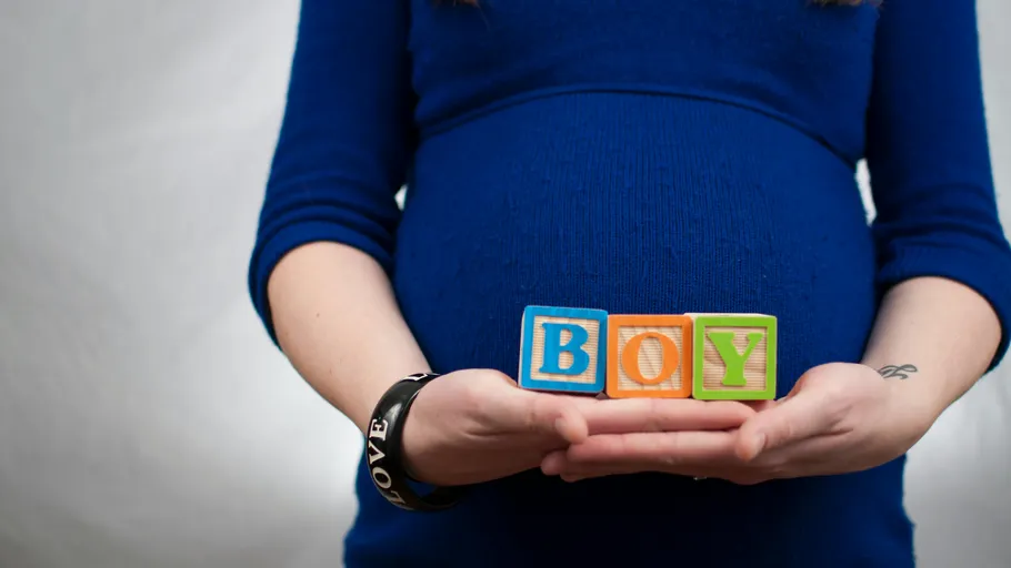 Pregnant woman holds blocks spelling "BOY".