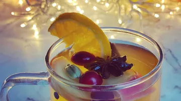 Hot beverage with orange, spices, cranberries, lights.