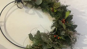 Grüner Kranz mit roten Beeren auf Tisch.