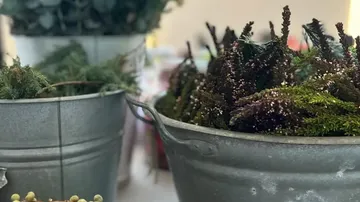 Metal buckets filled with foliage on table.