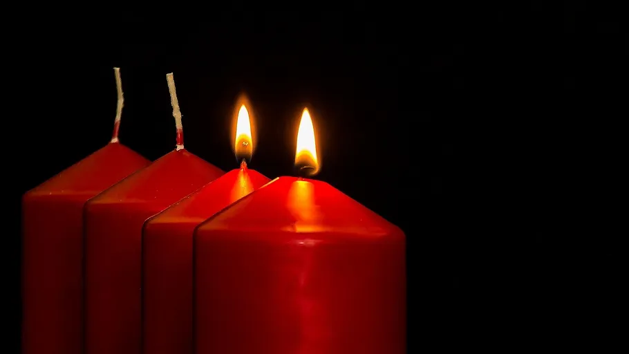 Drei rote Kerzen, zwei angezündet, vor schwarzem Hintergrund.