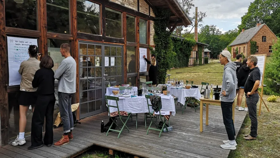 People writing on paper, outside rustic building.