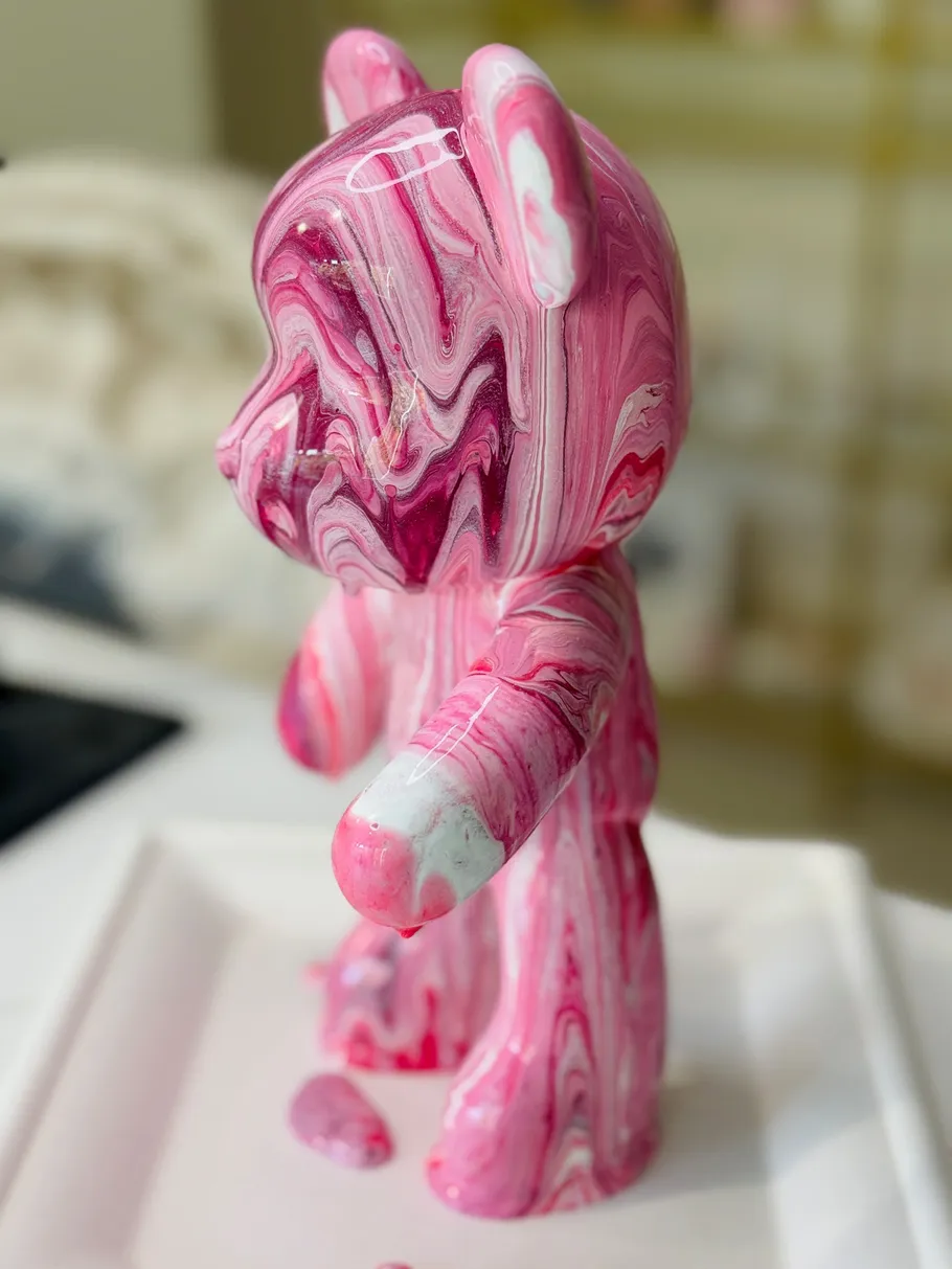 Pink bear sculpture with marbled paint indoors.