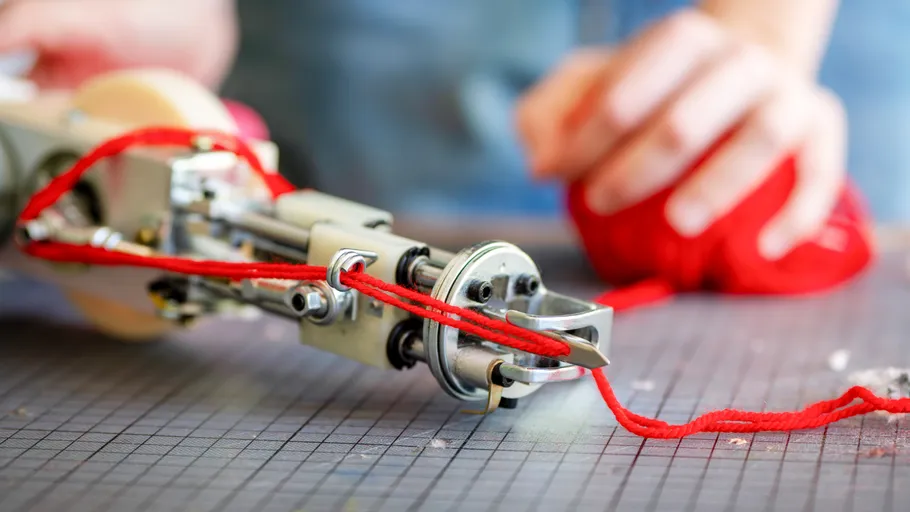Roboterhand strickt roten Faden drinnen.