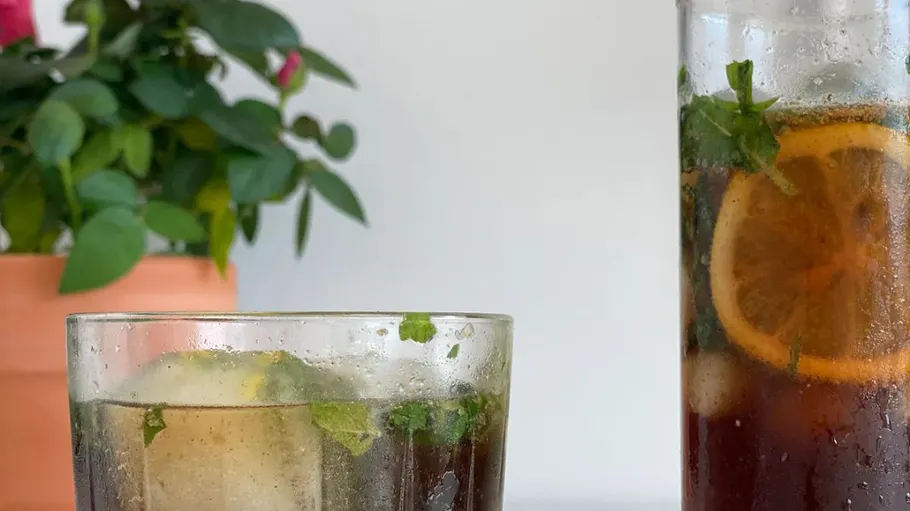 Glass and pitcher with iced drink, plant nearby.