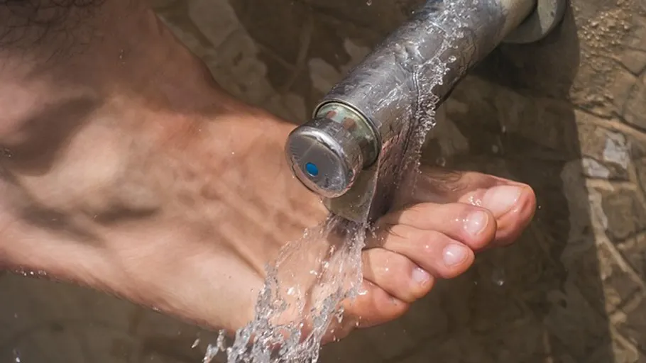 Fuß waschen unter einem Wasserhahn im Freien.