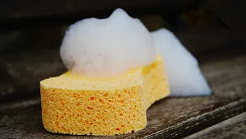 Gelber Schwamm mit Schaum auf Holzoberfläche.