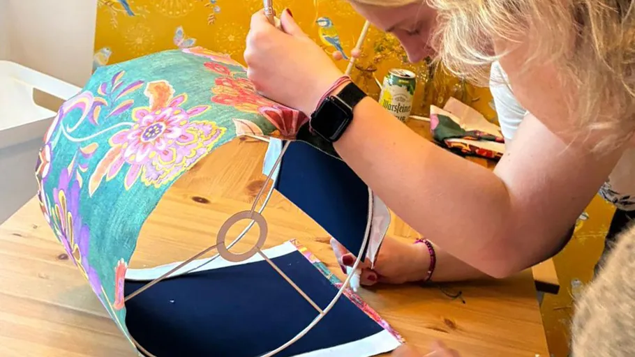 Person decorating lampshade, wooden table background.