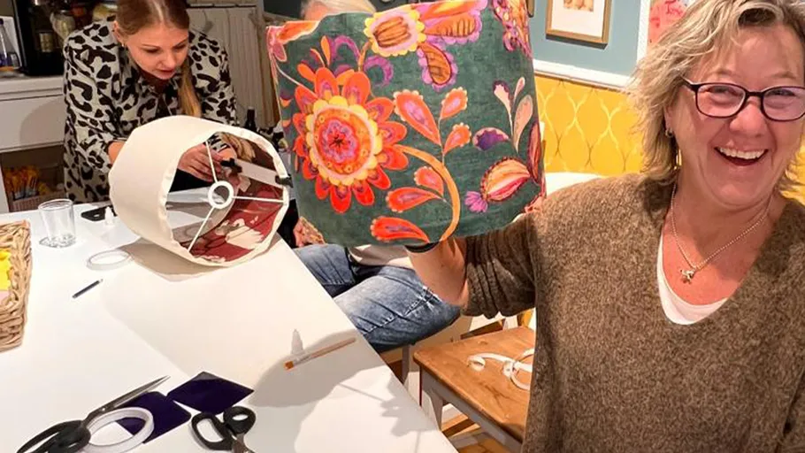 Smiling woman holds colorful lampshade in workshop.