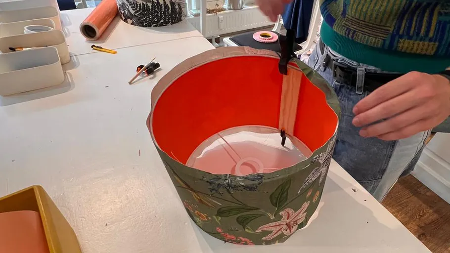 Person assembling a floral lampshade on table.