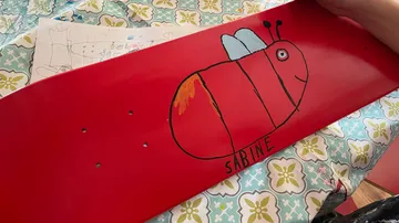 Red skateboard with hand-drawn insect design.
