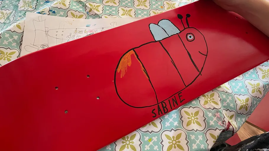 Hand holding red skateboard with bee drawing.