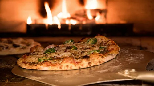 Pizza on peel in front of wood-fired oven.