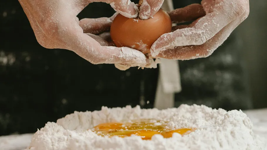 Hands cracking egg over flour pile.
