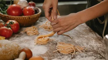 Hände formen hausgemachte Pasta auf bemehlter Fläche.