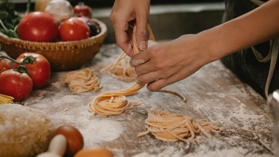 Hands shaping homemade pasta on floured surface.
