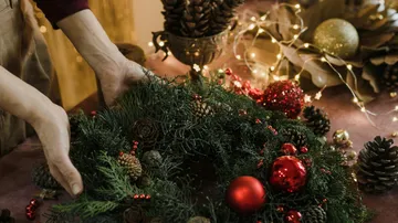 Hands arranging festive wreath with decorations.