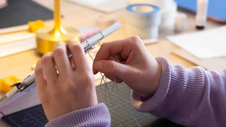 Hands weaving thread on a metal frame.