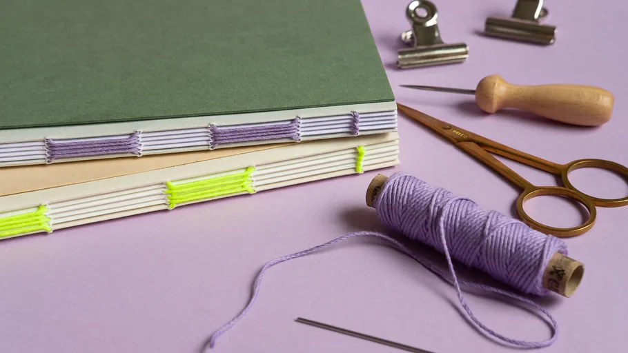 Thread, notebooks, and tools on purple surface.