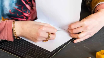 Hände nähen Papier auf schwarzem Tisch.