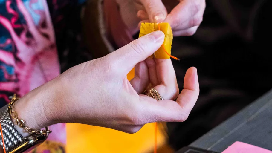 Hands sewing yellow fabric with needle.