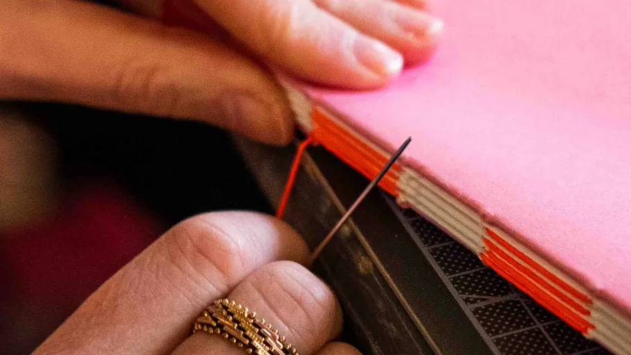 Hands sewing pink notebook binding.